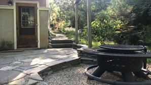 Zona de pati amb una barbacoa, escales de pedra cap a una porta i una estructura de pergola.
