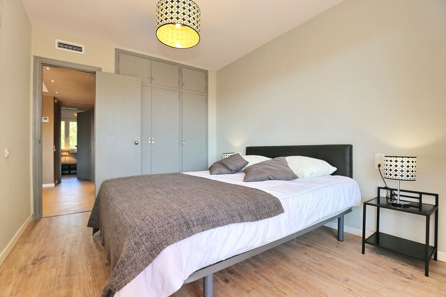 Une chambre à coucher comprenant un lit, une lampe de chevet, une armoire et un couloir menant à une autre pièce.