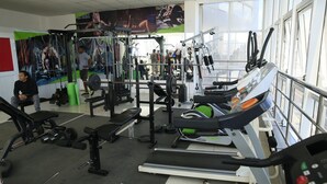 Een fitnessruimte met diverse trainingsapparaten, waaronder loopbanden, krachttoestellen en een squats rek.