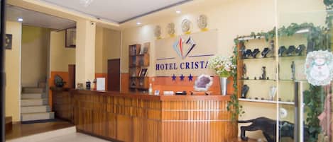 Un mostrador de recepción de hotel con encimera de madera, una araña y un cartel en la pared que dice "HOTEL CRISTAL".