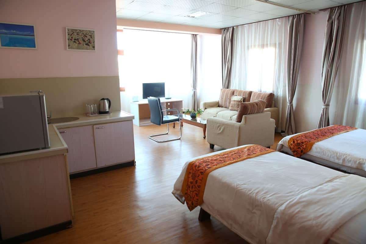 A hotel room with two beds, a desk, a chair, a television, and a kitchenette.