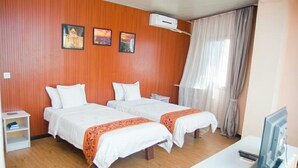 Een hotelkamer met twee bedden, een bureau, een televisie en een raam met gordijnen.