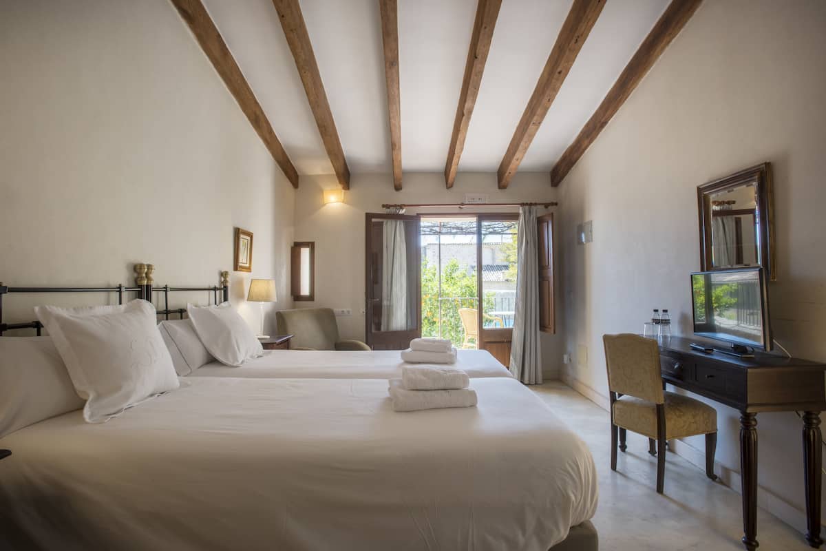 A hotel room with two beds, a desk, a chair, and a television.