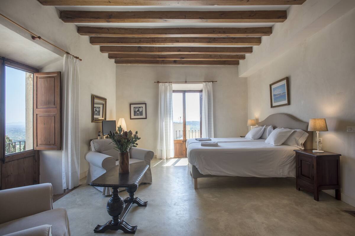 A bedroom with a bed, bedside tables, a chair, a table with a vase, and a window with curtains.