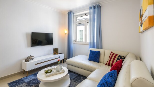 Un salon moderne avec un canapé beige, un téléviseur à écran plat fixé au mur, une console blanche et un tapis à motifs.