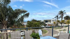 Un balcón con una mesa de vidrio, una planta en maceta y vistas a una zona residencial con casas y palmeras.