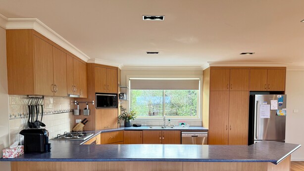 Una cocina moderna con armarios de madera, un refrigerador de acero inoxidable, una isla grande con taburetes de bar y un ventanal que proporciona luz natural.