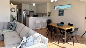 Et moderne køkken med hvide skabe, en central ø og et spiseområde med et træbord og stole.