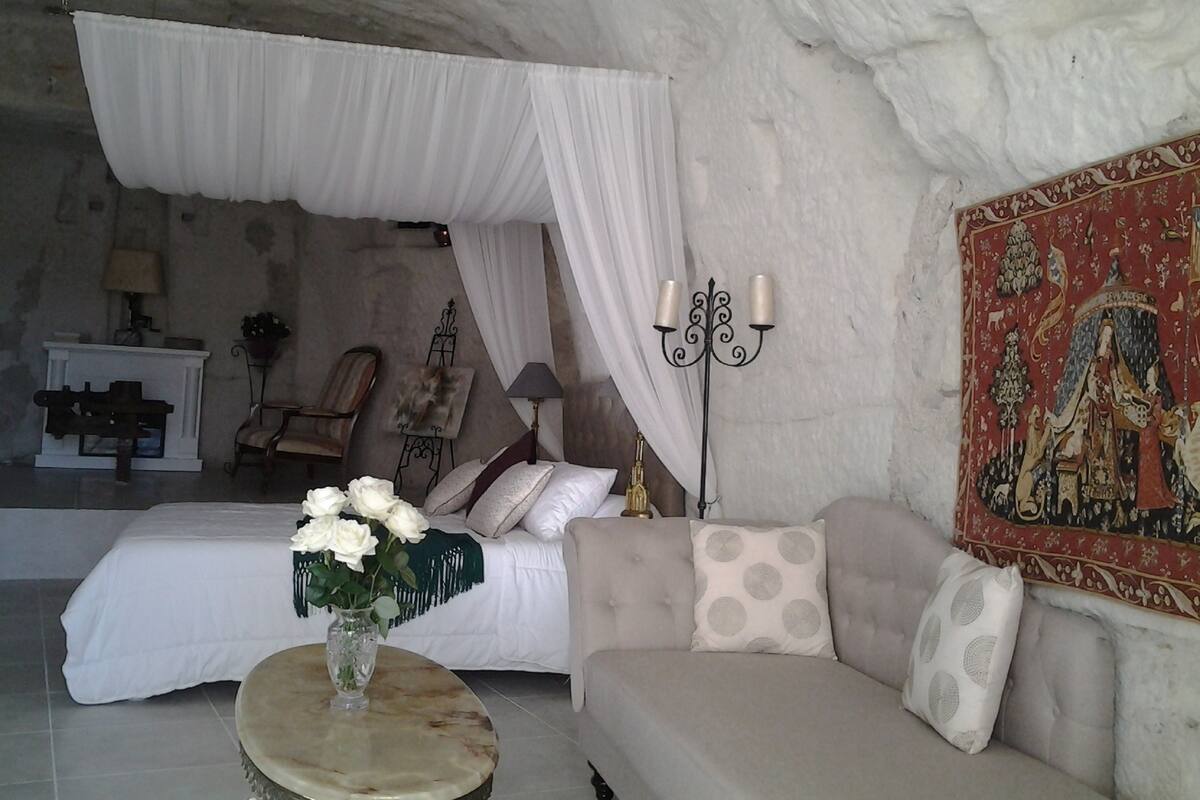 A bedroom with a bed, a sofa, a nightstand, a lamp, and a wall painting.