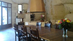 Un comedor con una gran mesa de madera, sillas, un florero con flores y una cocina al fondo.