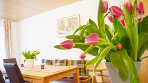 A dining area with a wooden table and chairs, a potted plant, and a vase with pink tulips. - Landhaus Valentin (Triberg im Schwarzwald)
