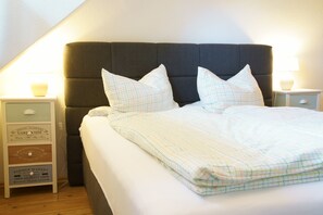 A neatly made bed with a checkered bedspread and two pillows, flanked by nightstands with lamps and a small sign.