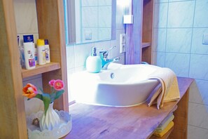 A bathroom with a white sink, a mirror, and toiletries on a shelf.