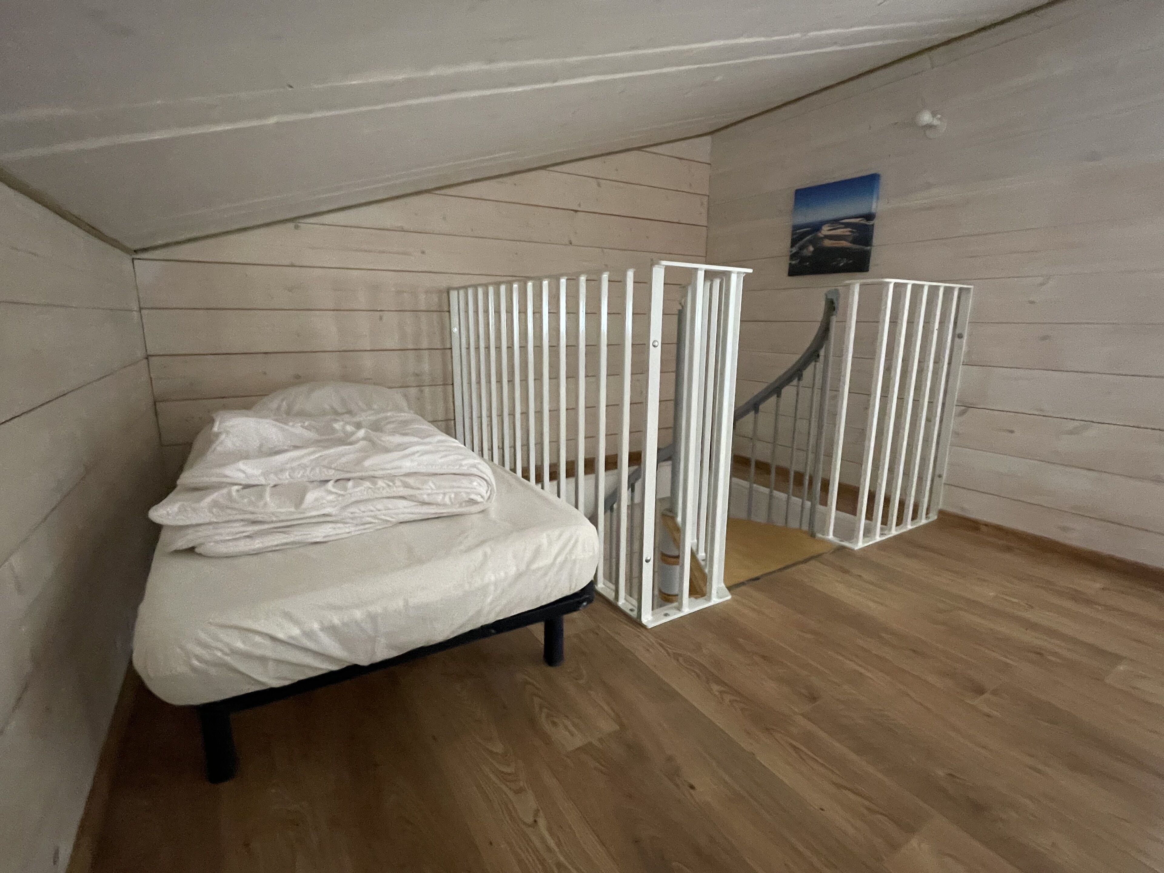 A small, single-bed room with a sloped ceiling and wooden walls.
