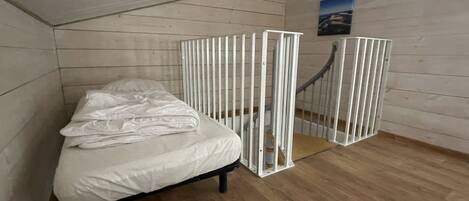 A small, single-bed room with a sloped ceiling and wooden walls.