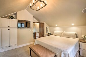 Une chambre à coucher avec un grand lit, un banc, une télévision et un luminaire fixé au plafond.