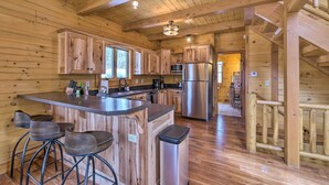 A wooden cabin interior with a kitchen area featuring wooden cabinets, a stainless steel refrigerator, and a bar stool area.