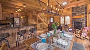 A wooden cabin interior with a dining area, kitchen, and a stone fireplace.