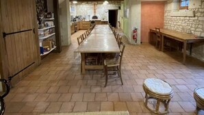 A rustic dining area with a long wooden table and chairs, stone walls, and exposed wooden beams. - Pic Epeiche Gite (Lerné)