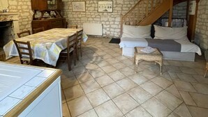 A rustic room with exposed wooden beams, a stone wall, a dining table with chairs, a sofa, and a small table with a lamp. - Pic Epeiche Gite (Lerné)