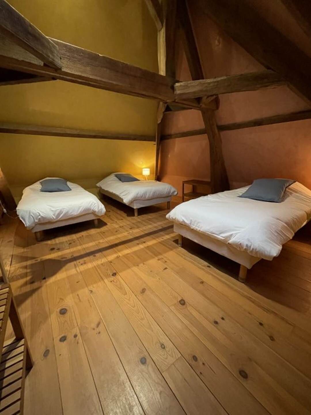 Un dormitorio abrigado en el ático, con tres camas de madera, techo inclinado y paredes de color amarillo cálido.