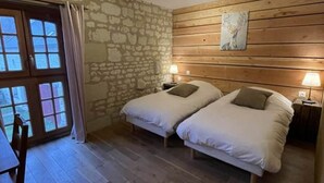 A bedroom with two beds, stone walls, wooden paneling, a table, and a chair. - Pic Epeiche Gite (Lerné)