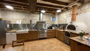 A rustic kitchen with stone walls, wooden cabinets, a gas stove, a built-in oven, and a brick floor. - Pic Epeiche Gite (Lerné)