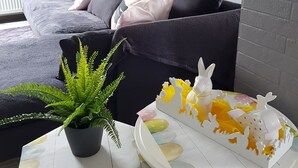 A modern living room with a grey sofa, white and black cushions, a small white table with a potted plant, and a decorative white table runner. - Beautiful apartment with large sun terrace - Apartment Elegance (Höheischweiler)