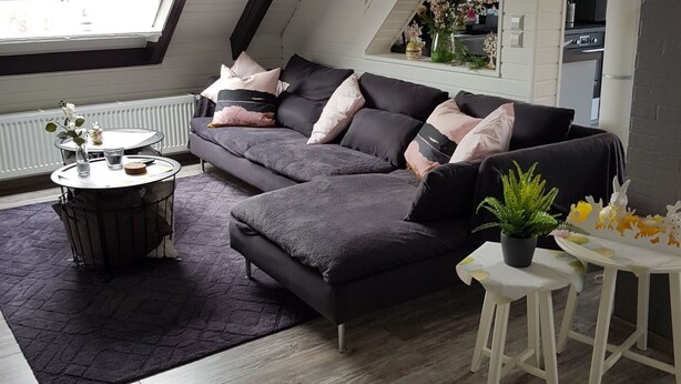 A modern loft-style living room with a sectional sofa, a round coffee table, and a small dining table. The room features exposed wooden beams, a skylight, and a view of the kitchen. - Beautiful apartment with large sun terrace - Apartment Elegance (Höheischweiler)