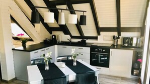 A modern kitchen with a dining area, featuring a white table, black chairs, and pendant lights. - Beautiful apartment with large sun terrace - Apartment Elegance (Höheischweiler)