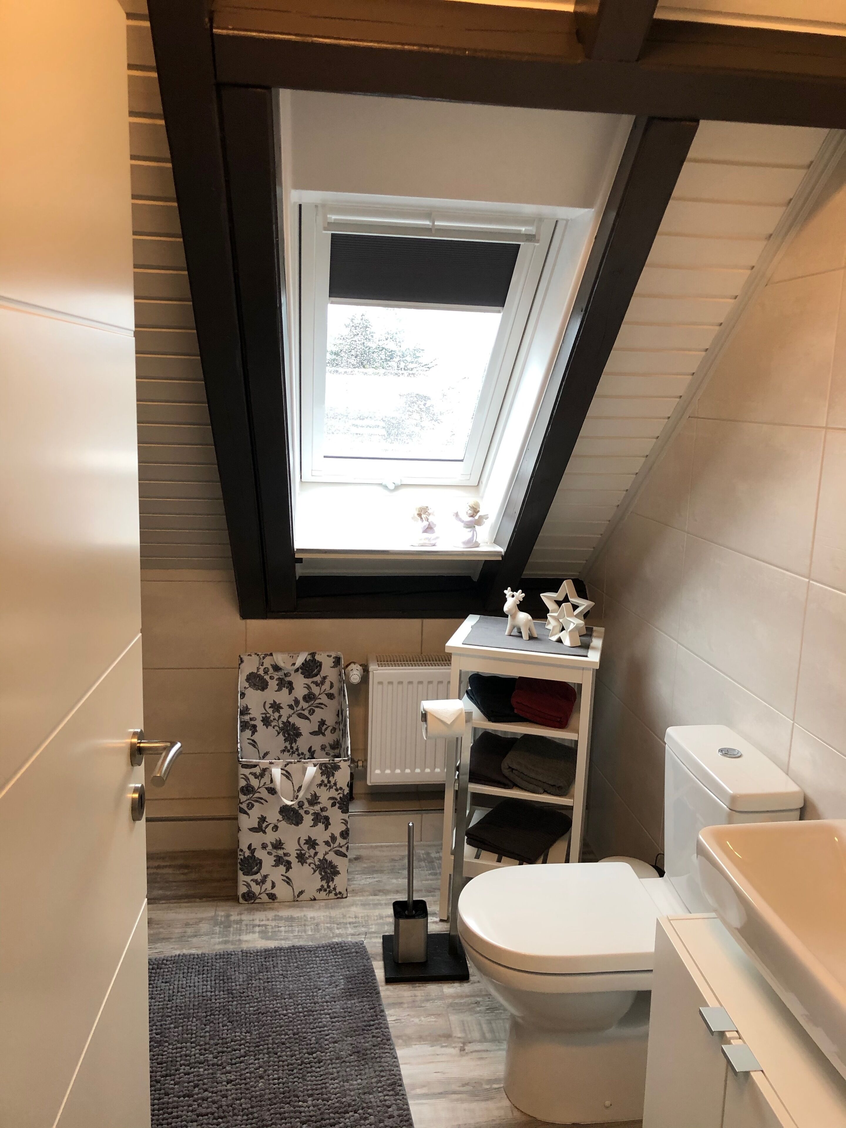 Ein kleines, modernes Badezimmer mit Dachfenster, Toilette, Heizkörper und Ablage für Toilettenartikel.