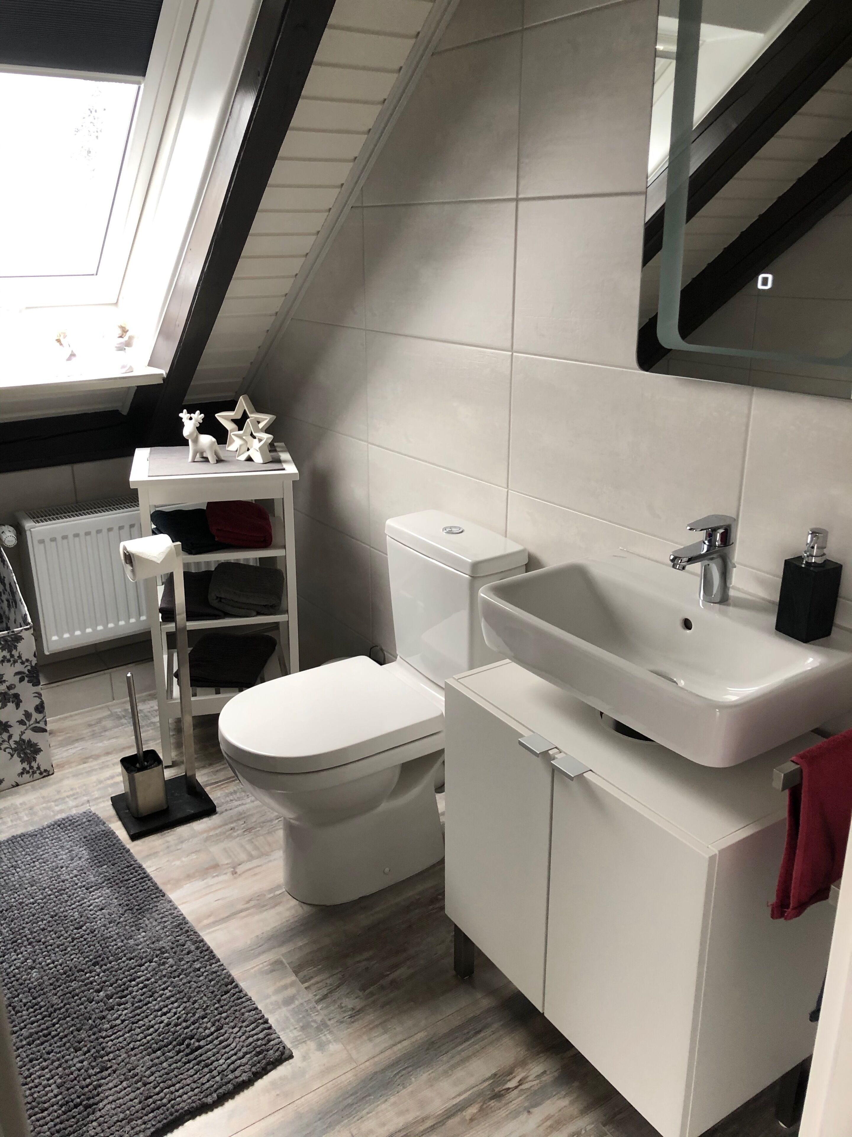 Un baño moderno con tragaluz, sanitarios blancos, radiador y alfombra gris.