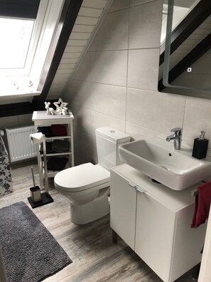 Ein modernes Badezimmer mit Oberlicht, weißen Armaturen, einem Heizkörper und einem grauen Teppich.
