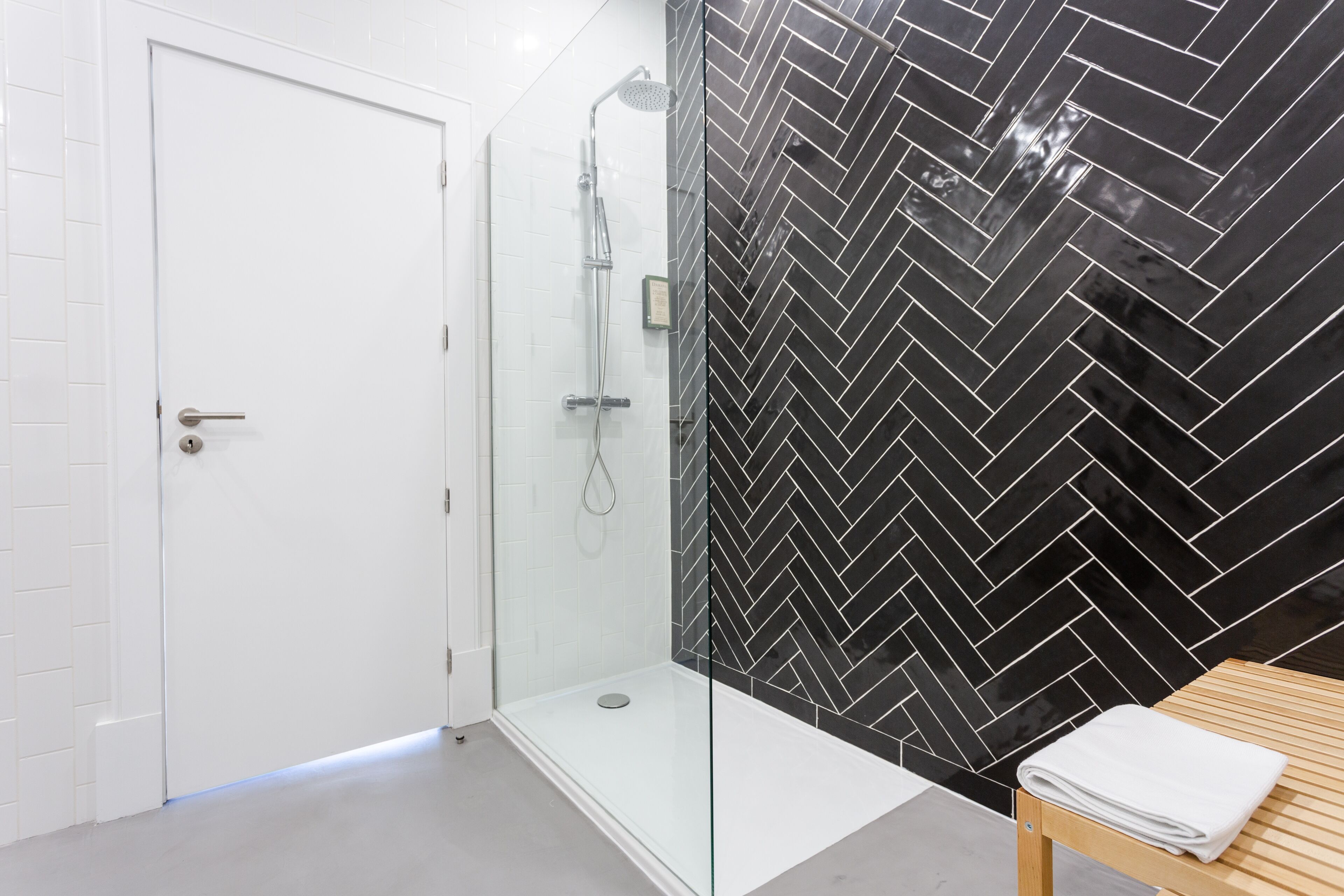 A modern bathroom with a glass-enclosed shower, white tiled walls, and a black herringbone-patterned wall.