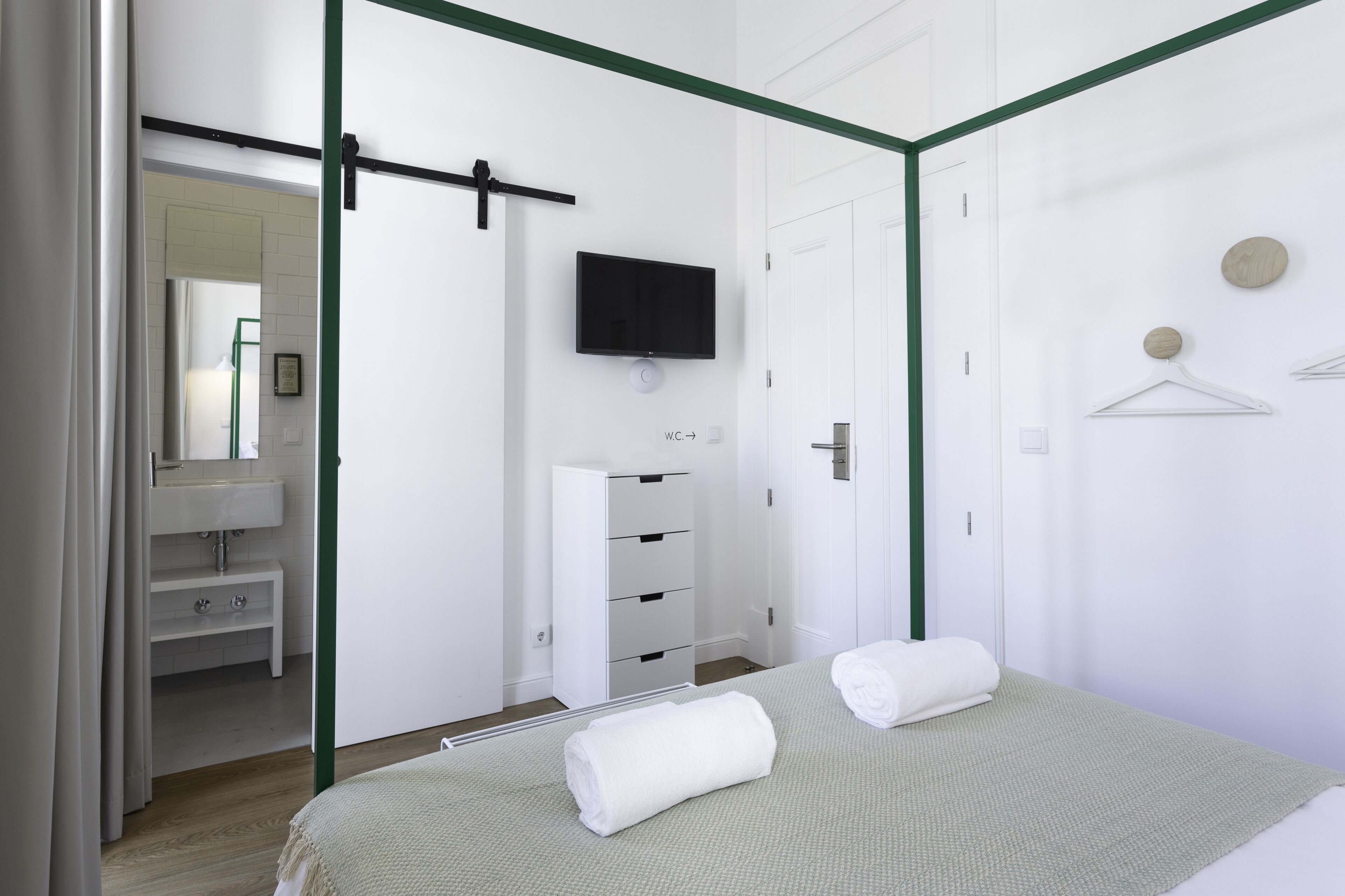 Een slaapkamer met een bed, een aan de muur bevestigde televisie, een kledingkast en een badkamer die door een open deur zichtbaar is.