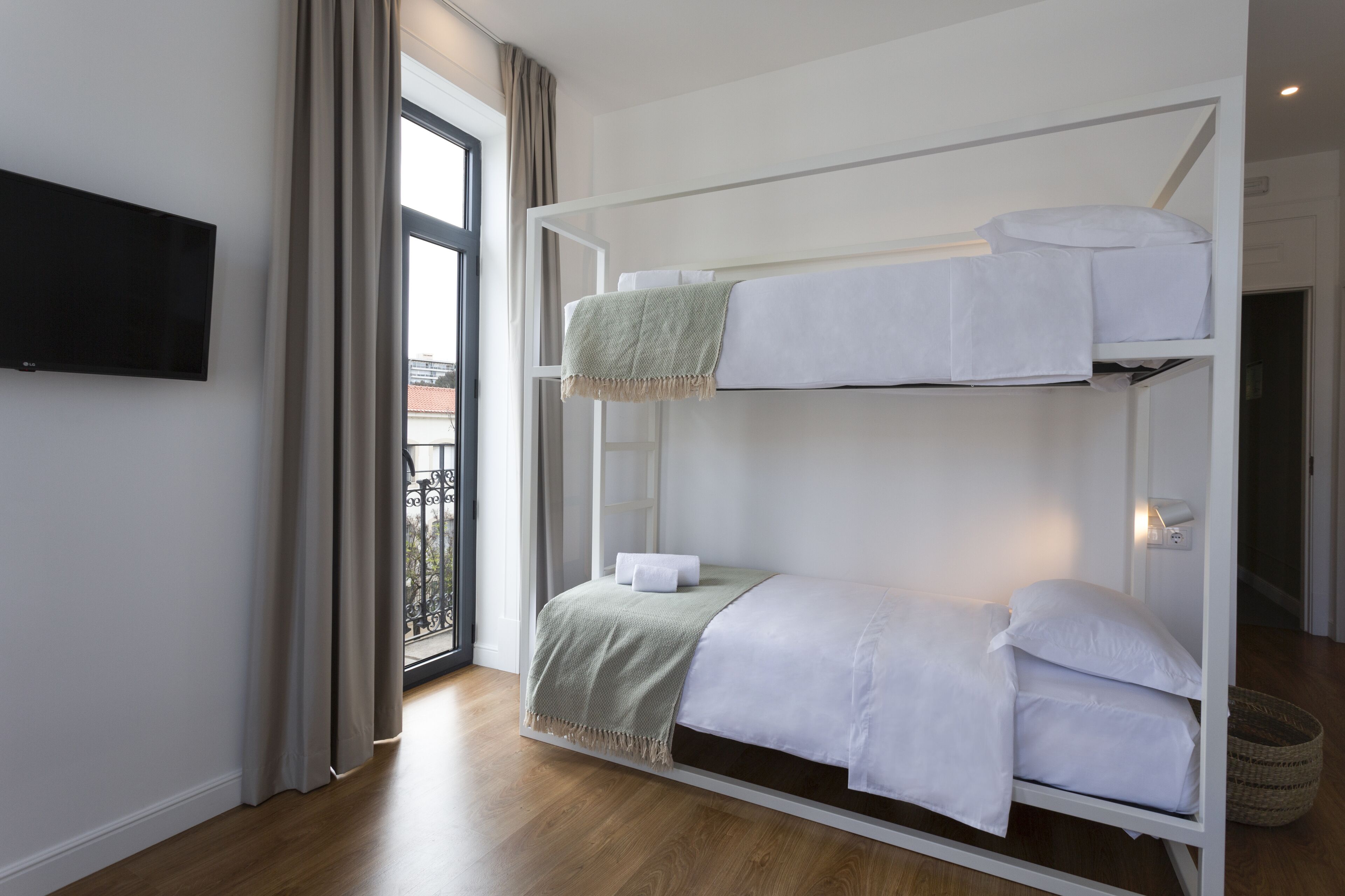 A bunk bed room with a TV on the wall, a window with curtains, and a balcony view.