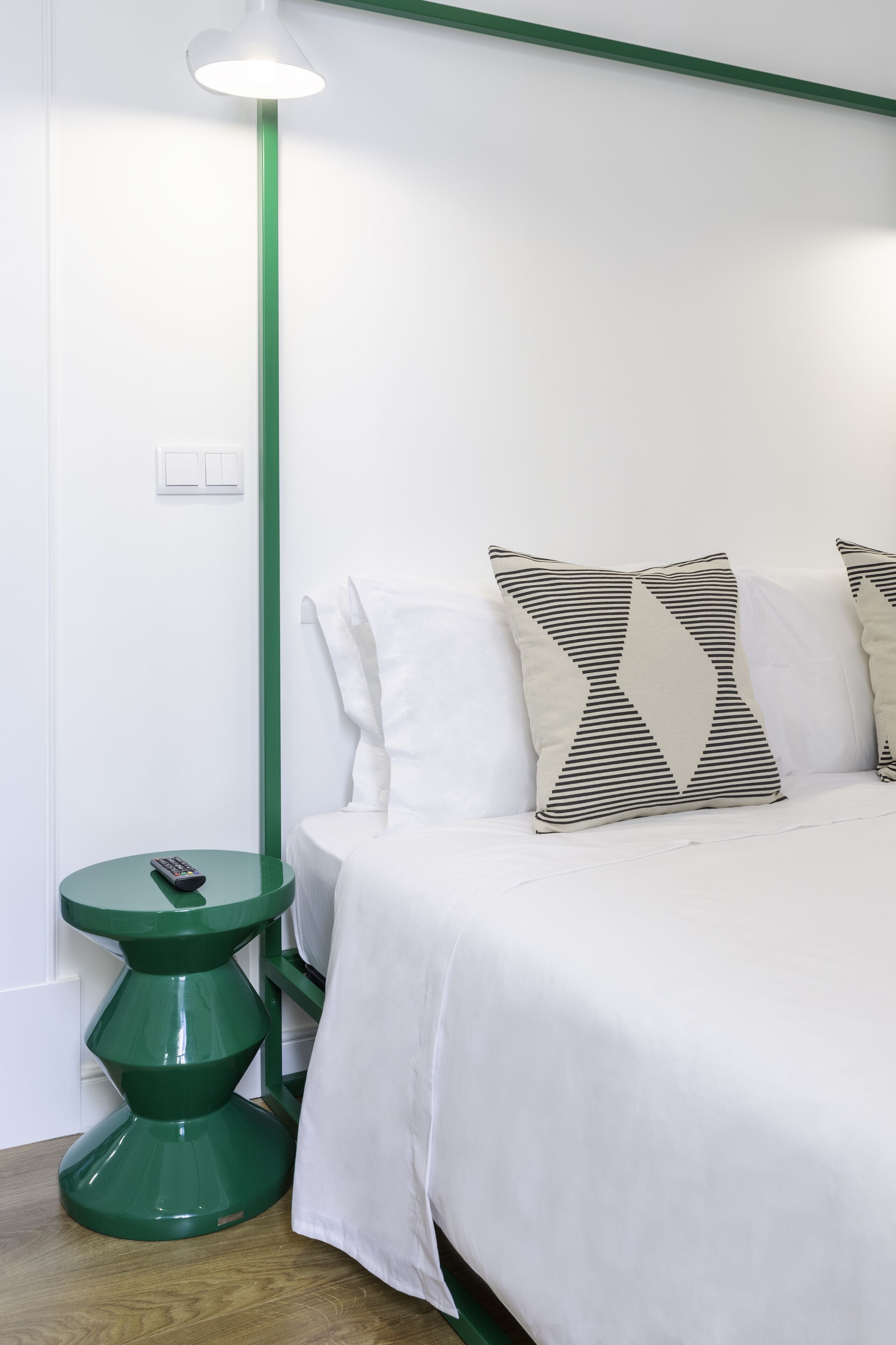 Ein ordentlich eingerichtetes Schlafzimmer mit einem Bett, Kissen, einem grünen Nachttisch und einer Stehlampe.