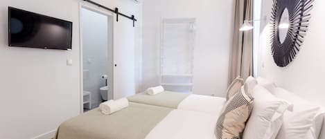 Ett modernt hotellrum med en säng, en TV, en dusch och en väggmonterad lampa.