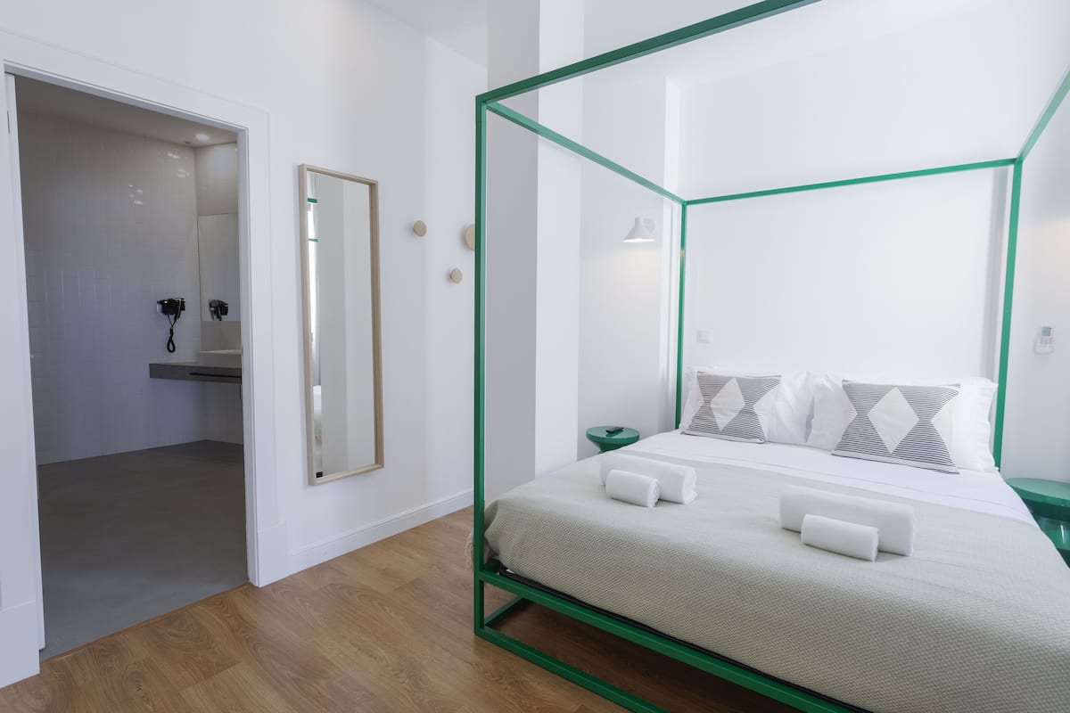 A modern bedroom with a four-poster bed, a green-framed canopy, and a wooden floor.
