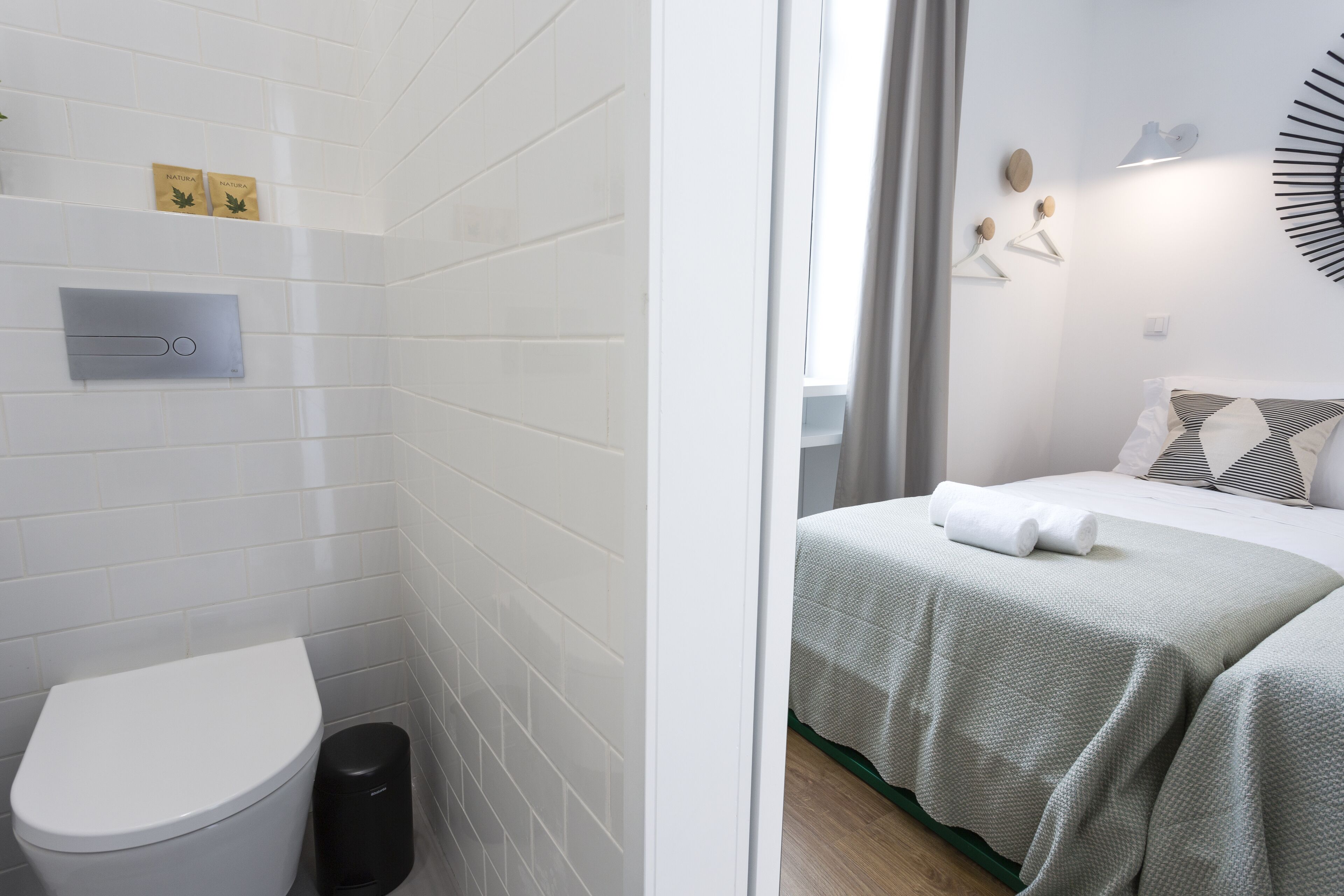 A bathroom with white tiles, a toilet, and a trash bin.