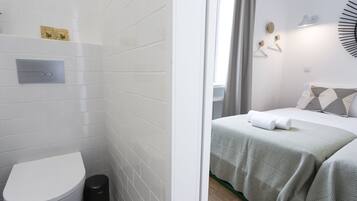 A bathroom with white tiles, a toilet, and a trash bin.