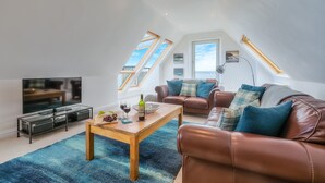 Ein modernes Wohnzimmer mit Fernseher, Couchtisch aus Holz, Ledersofas und Dachfenstern.