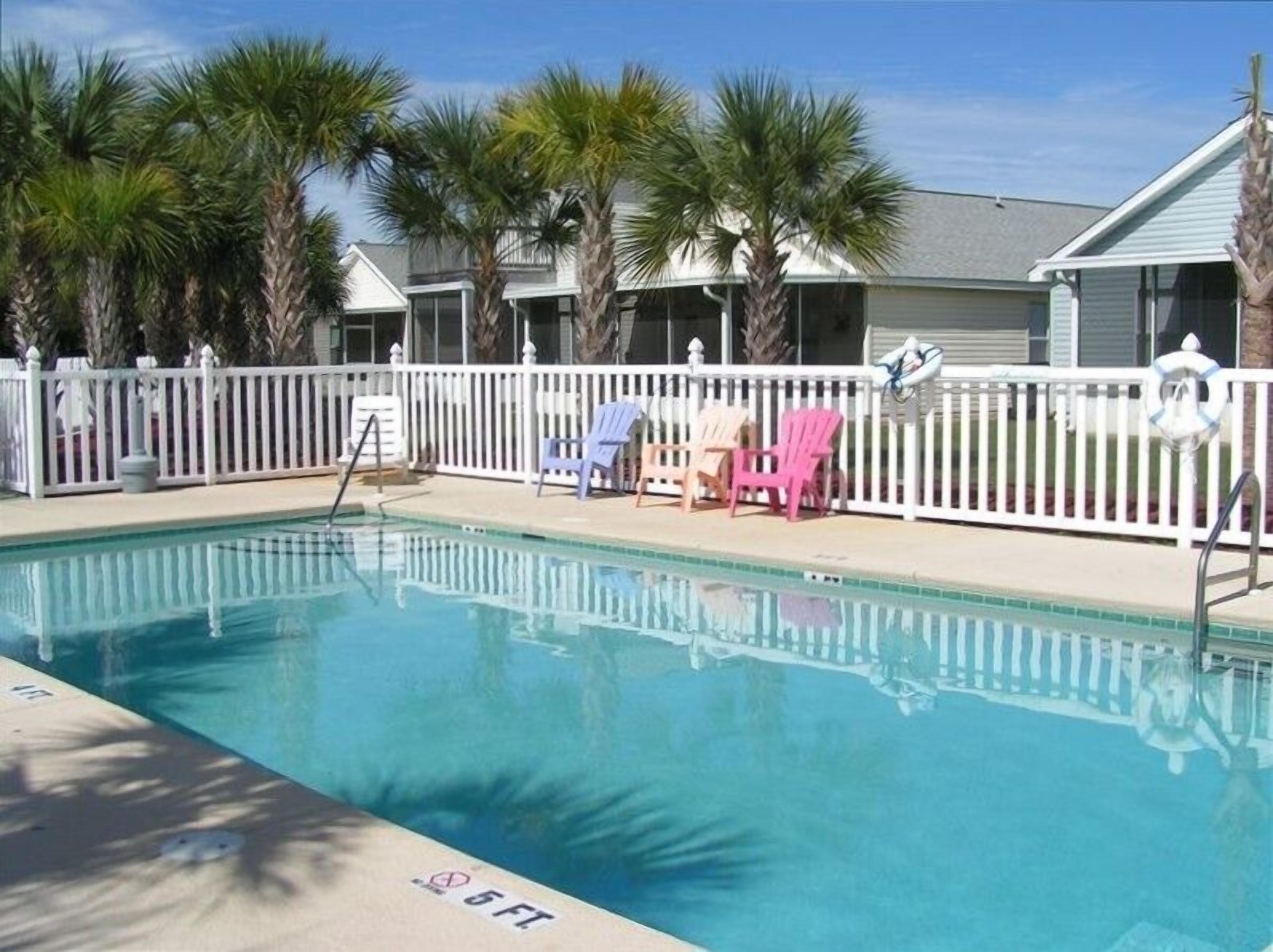 A swimming pool with a white fence, palm trees, and beach chairs.