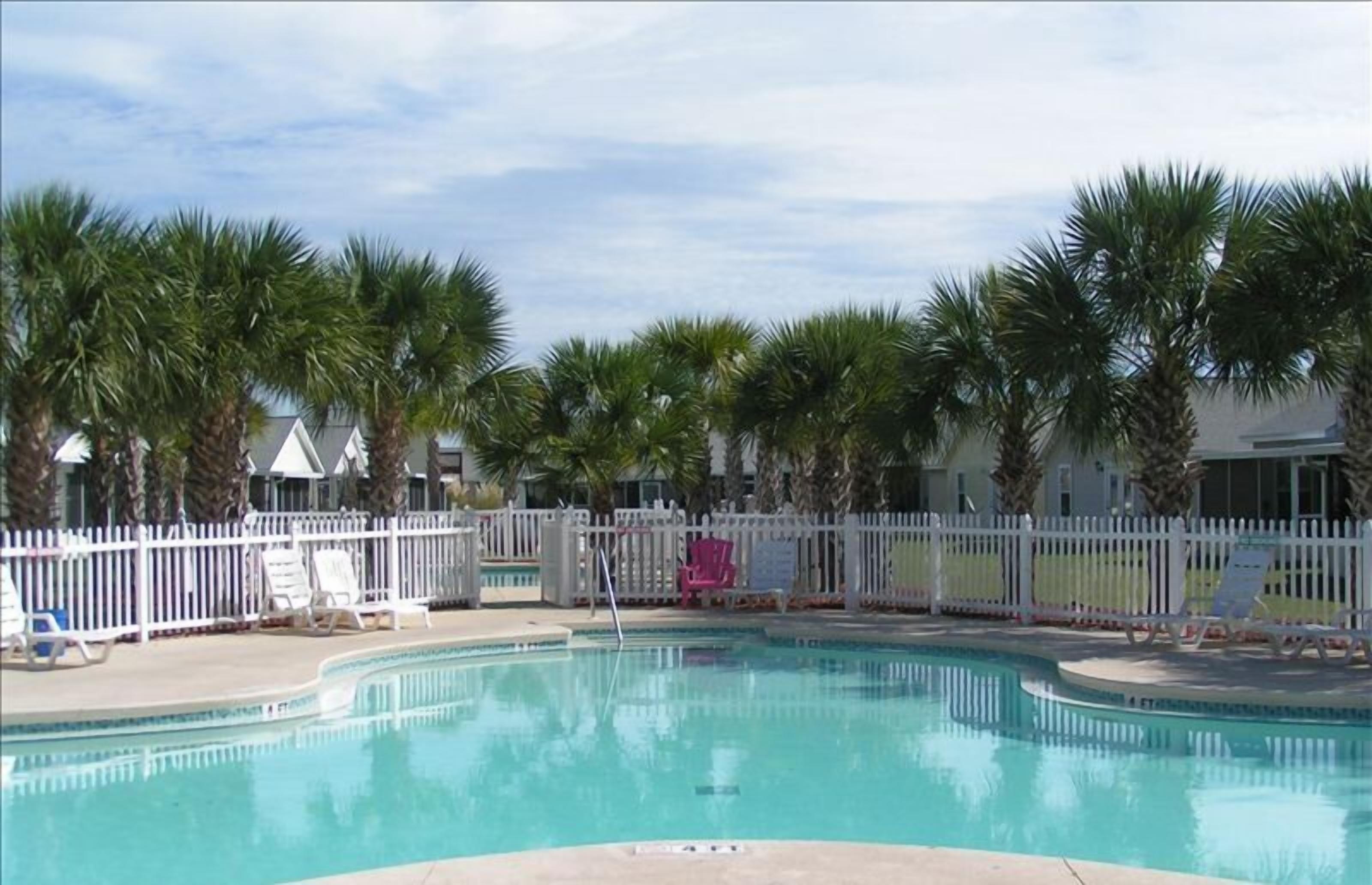 A swimming pool with palm trees and a white fence.