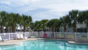 Une piscine bordée de palmiers et entourée d’une clôture blanche.