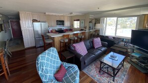 A spacious living room with a leather sofa, a blue armchair, and a glass coffee table. A kitchen with a central island and wooden cabinets is adjacent. - Rarely Available Oceanfront Penthouse (San Diego)
