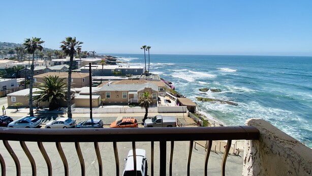 A coastal view with a balcony overlooking a parking area and ocean waves. - Rarely Available Oceanfront Penthouse (San Diego)