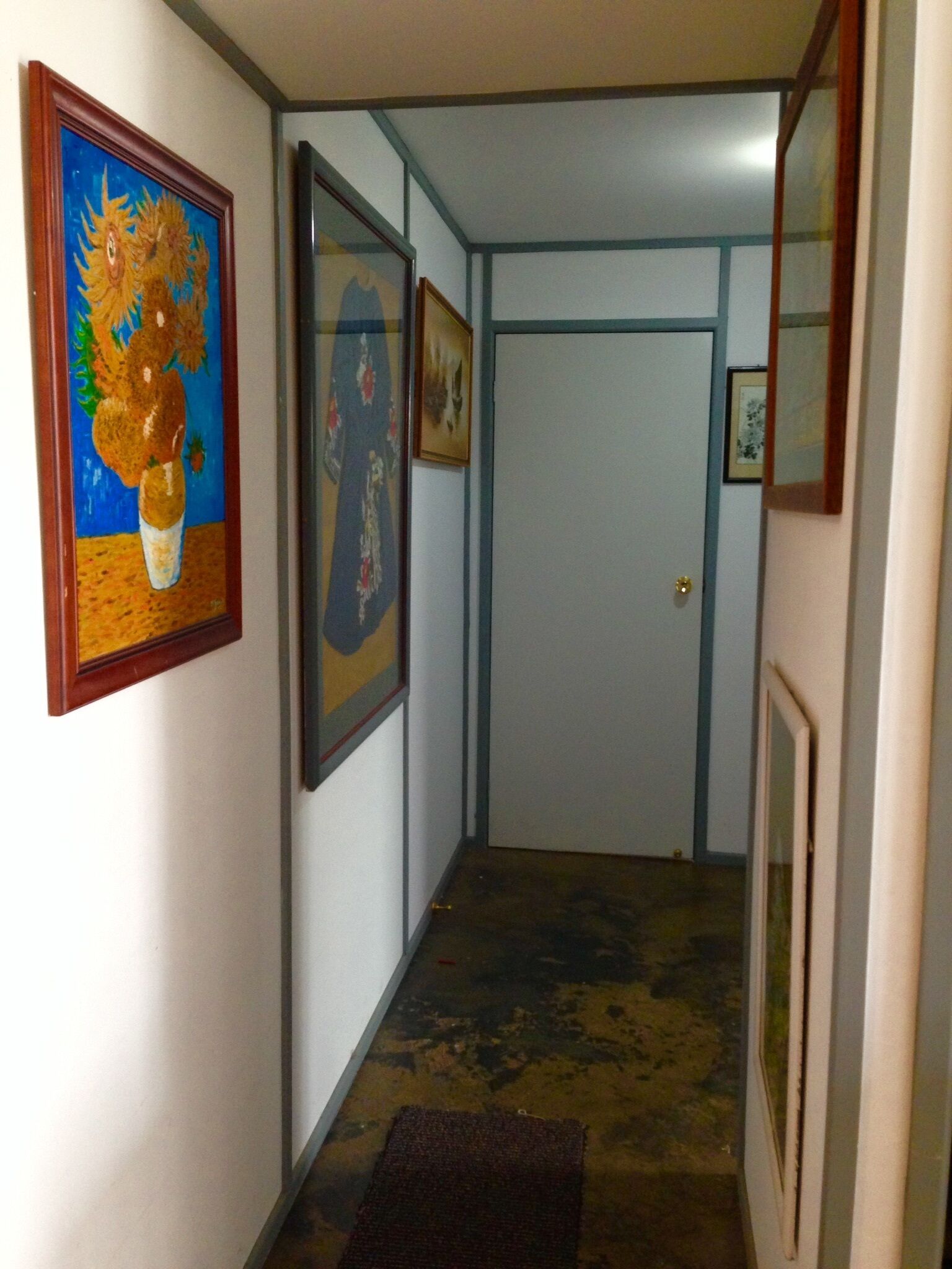 A hallway with a door at the end, framed artwork on the walls, and a carpeted floor.
