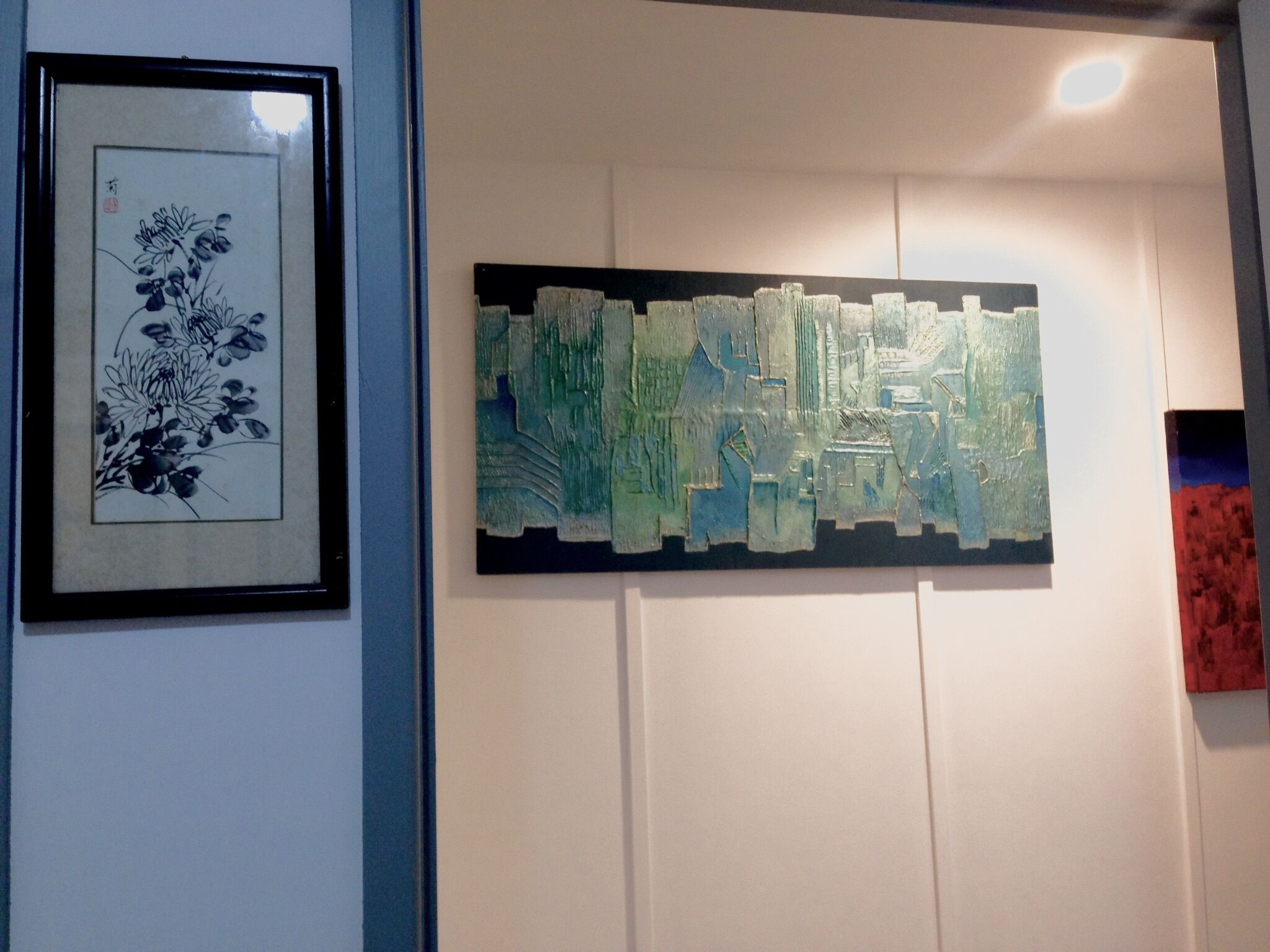 A wall with two artworks: a framed black and white floral print and a textured abstract painting.