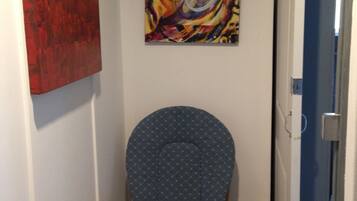 A hallway with a blue upholstered chair, a red abstract painting, and a colorful abstract painting on the wall.